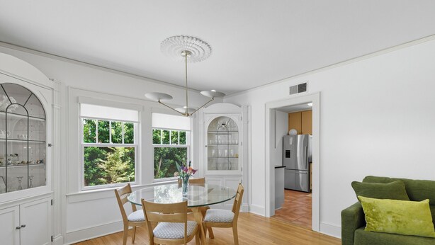 A dining area with a glass table and chairs, a chandelier, and a view of the outdoors through large windows. - Historic Cottage Meets Modern Comfort Near FSU (Tallahassee)