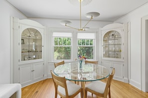 Une salle à manger avec une table ronde en verre, des chaises en bois et des meubles de rangement blancs dotés de portes en verre.