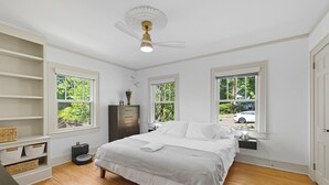 A bedroom with a bed, two windows, a ceiling fan, and a nightstand. - Historic Cottage Meets Modern Comfort Near FSU (Tallahassee)