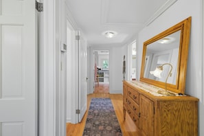 Un couloir avec une commode en bois, un miroir et un tapis à motifs.