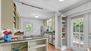 A modern kitchen with white cabinetry, a granite countertop, and a dining area with a wooden chair. - Historic Cottage Meets Modern Comfort Near FSU (Tallahassee)
