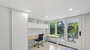 A modern office space with a desk, chair, and large windows. - Historic Cottage Meets Modern Comfort Near FSU (Tallahassee)