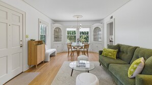 A bright, well-lit living room with a glass coffee table, a green sofa, and a dining area with wooden chairs and a glass table. - Historic Cottage Meets Modern Comfort Near FSU (Tallahassee)