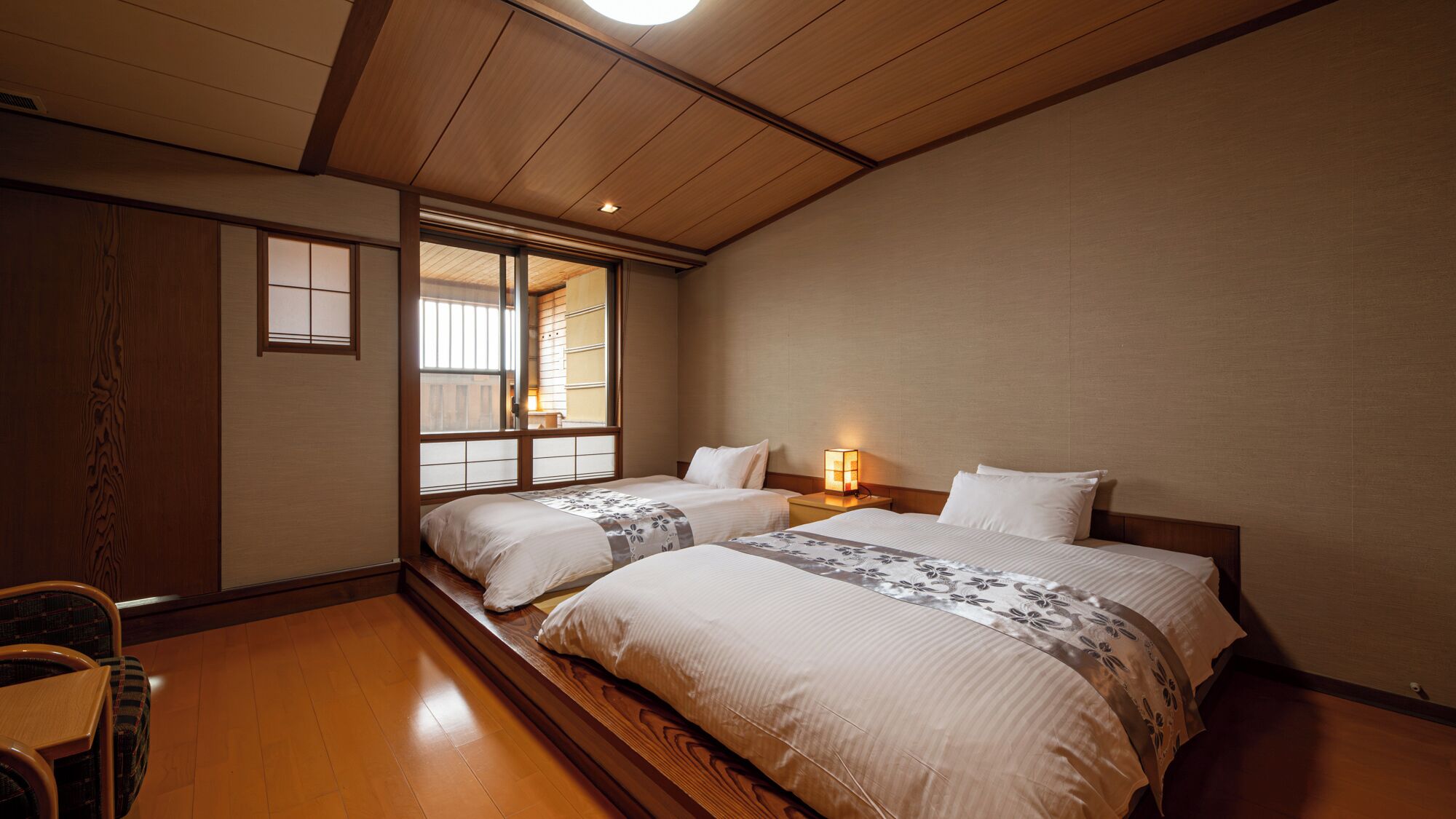 A traditional Japanese-style room with two beds, a wooden floor, and a sliding shoji screen window.