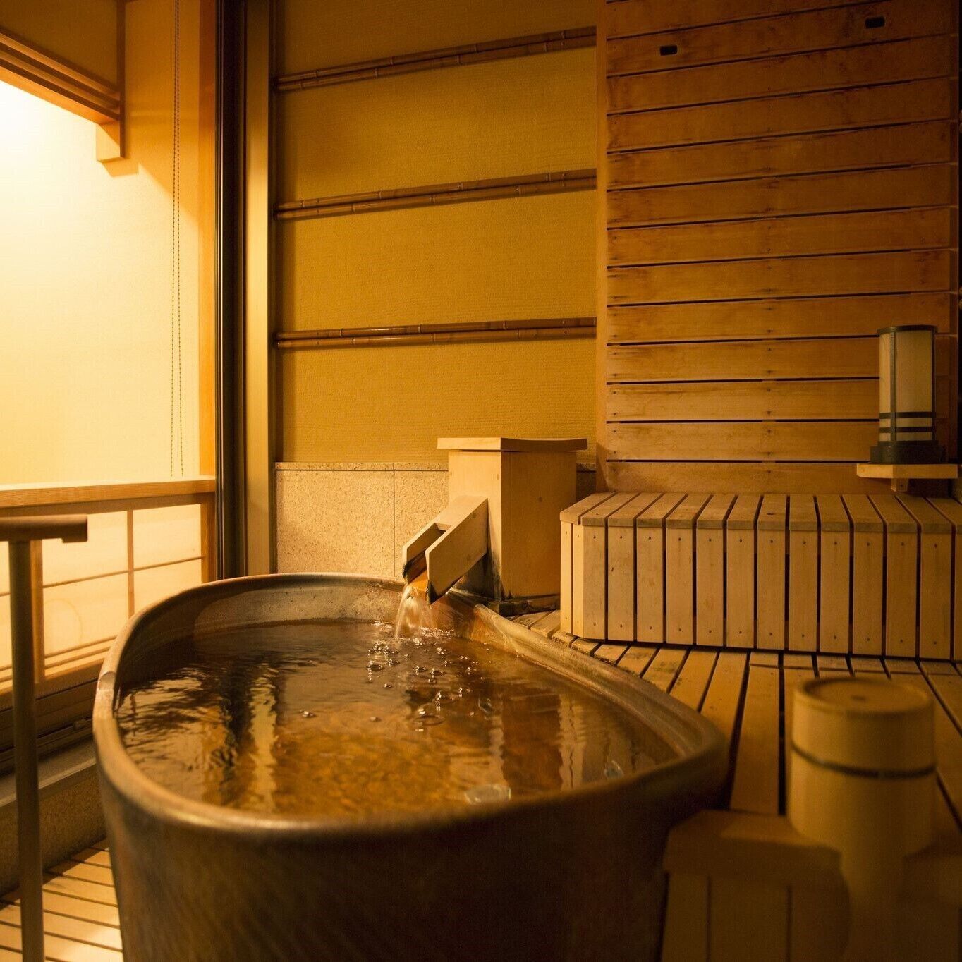A hot spring bath with a wooden bench and a small table, surrounded by wooden paneling.