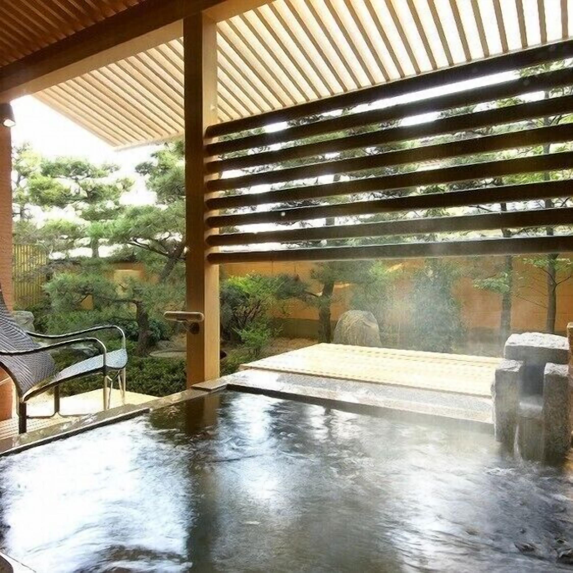 A hot spring area with wooden beams, a stone bench, and a view of trees.