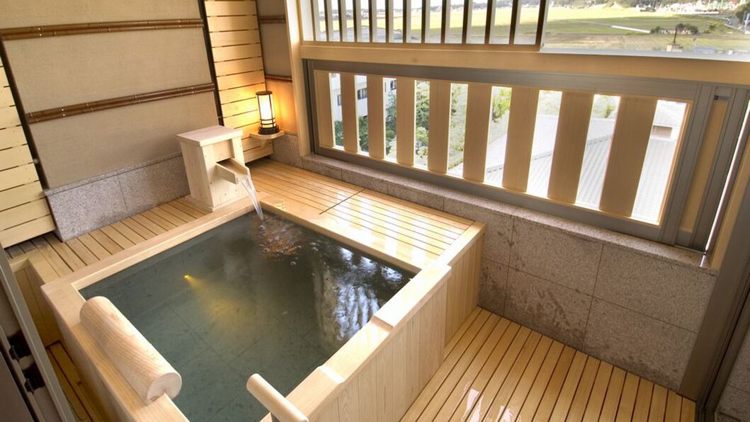 A hot spring bath with wooden flooring, a bench, and a view through a window.