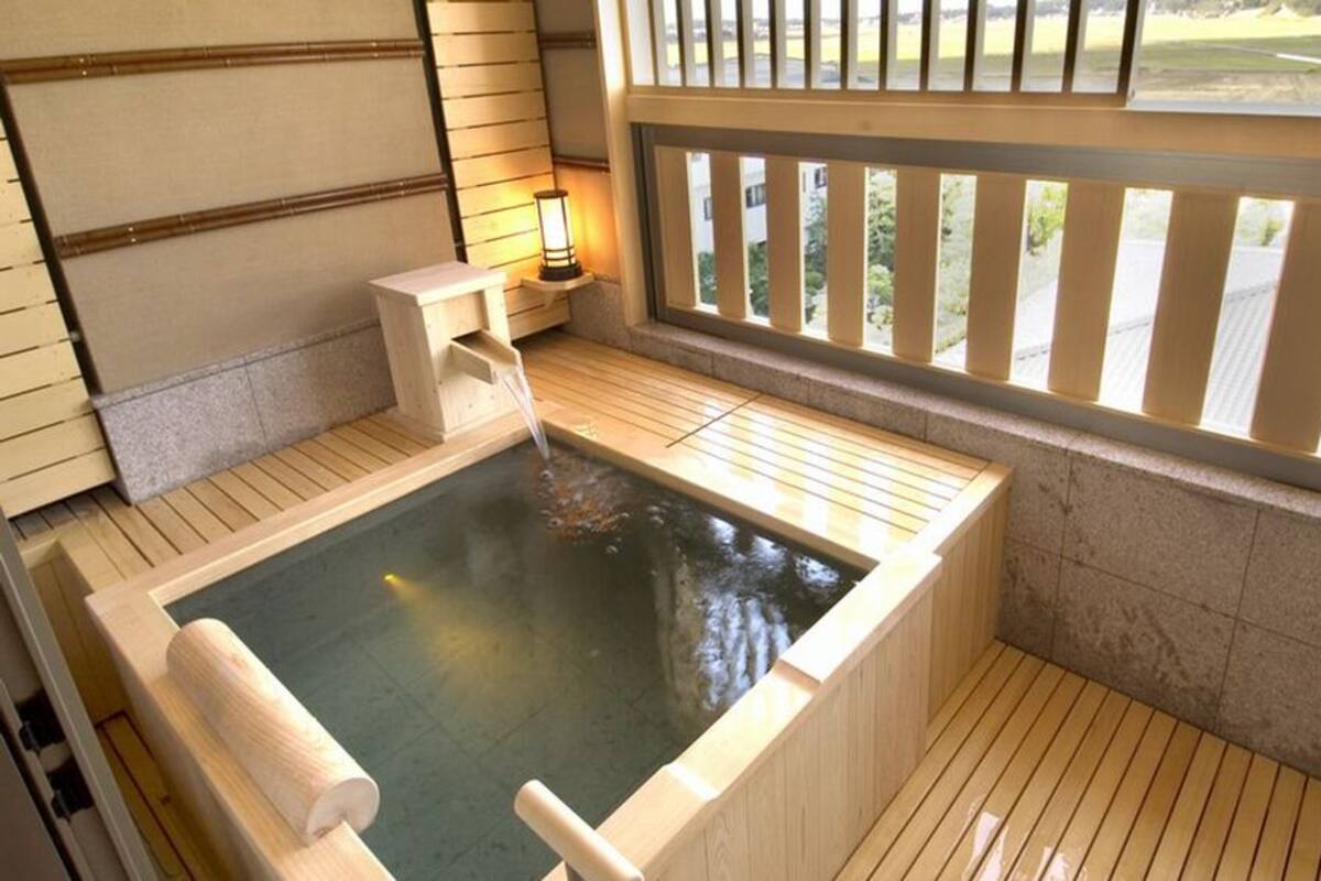 A hot spring bath with wooden flooring, a bench, and a view through a window.