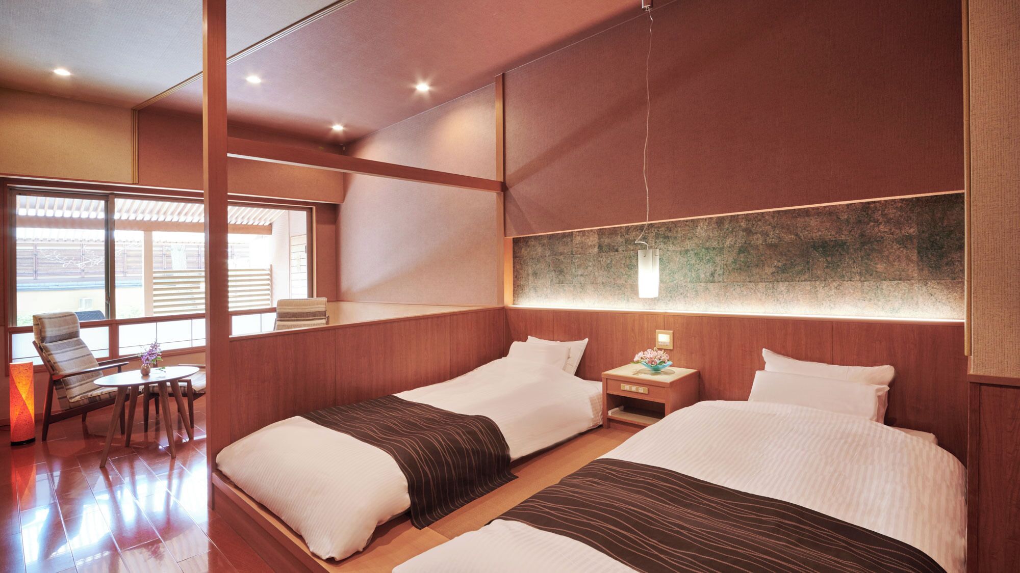 A hotel room with two beds, a small table, a chair, and a large window.