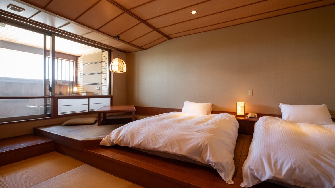 A hotel room with two beds, a bench, a large window, and a hanging light fixture.