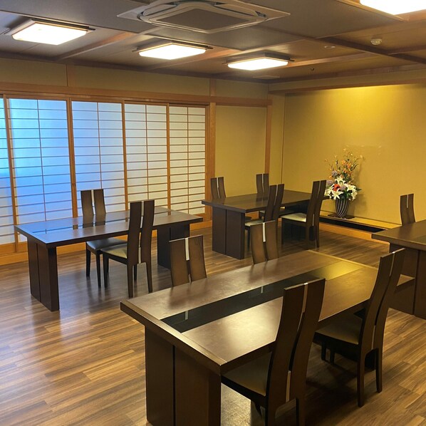 A conference room with wooden tables and chairs, large windows with a view, and a vase with flowers on the wall. - Awara Onsen Mimatsu (Awara)