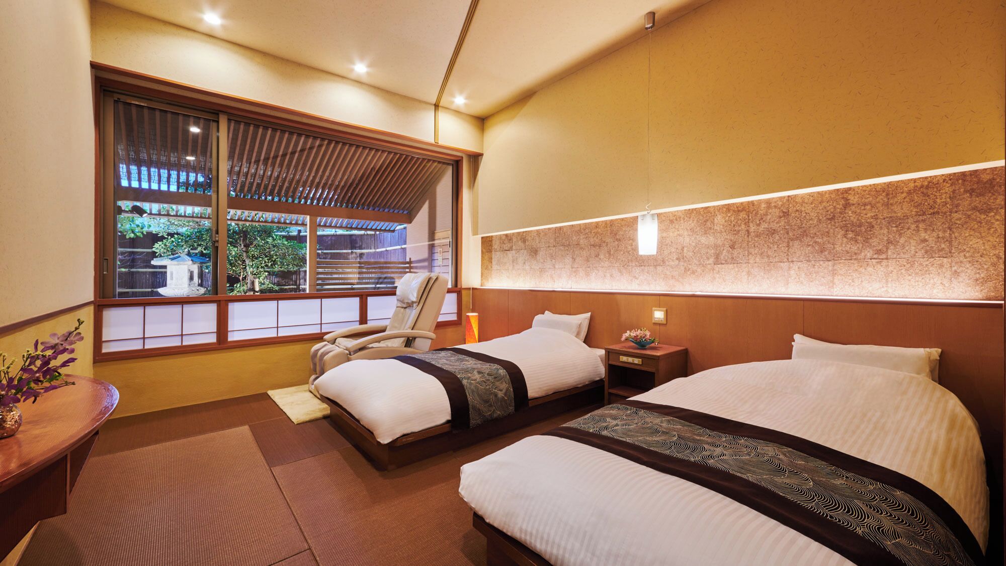 A hotel room with two beds, a sitting area with a chair, a small table, and a view of the outside.