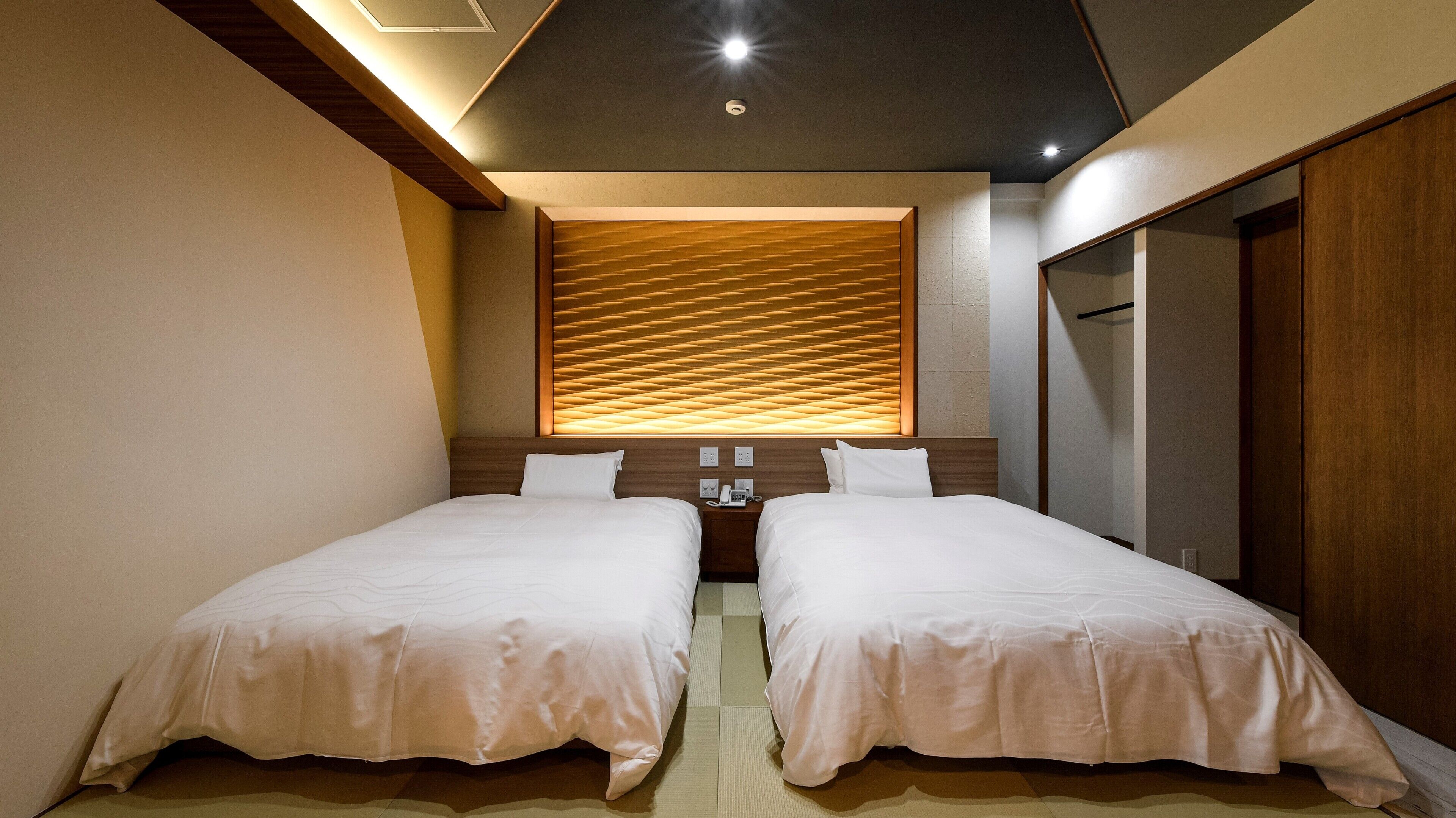 A hotel room with two beds, a wooden headboard, a wall-mounted phone, and a small bedside table.