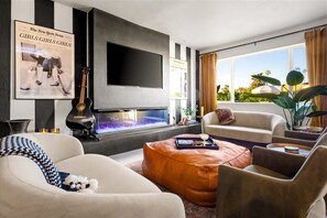 A modern living room with a fireplace, comfortable seating, a flat-screen TV, and a view of the outdoors.