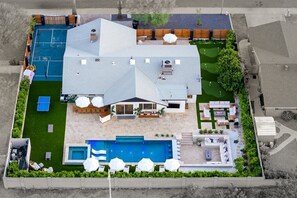 Ein modernes Haus mit großem Garten, inklusive Swimmingpool, Tennisplatz und einer Terrasse mit Gartenmöbeln.