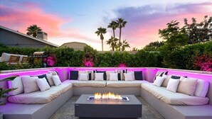 A modern outdoor seating area with a built-in fire feature, surrounded by lush greenery and palm trees. - Old Town's  Luxury Oasis - 16+ Guests, Designed for entertainment & relaxation. (Scottsdale)