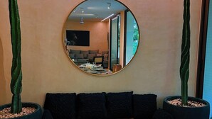 A modern living room with a round mirror, a wooden dining table set with plates and glasses, a dark sofa, and two large potted cacti. - Casa libre  (Tulum)