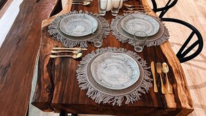 A dining table set with plates, glasses, and cutlery, surrounded by chairs and a sofa in a modern living room. - Casa libre  (Tulum)