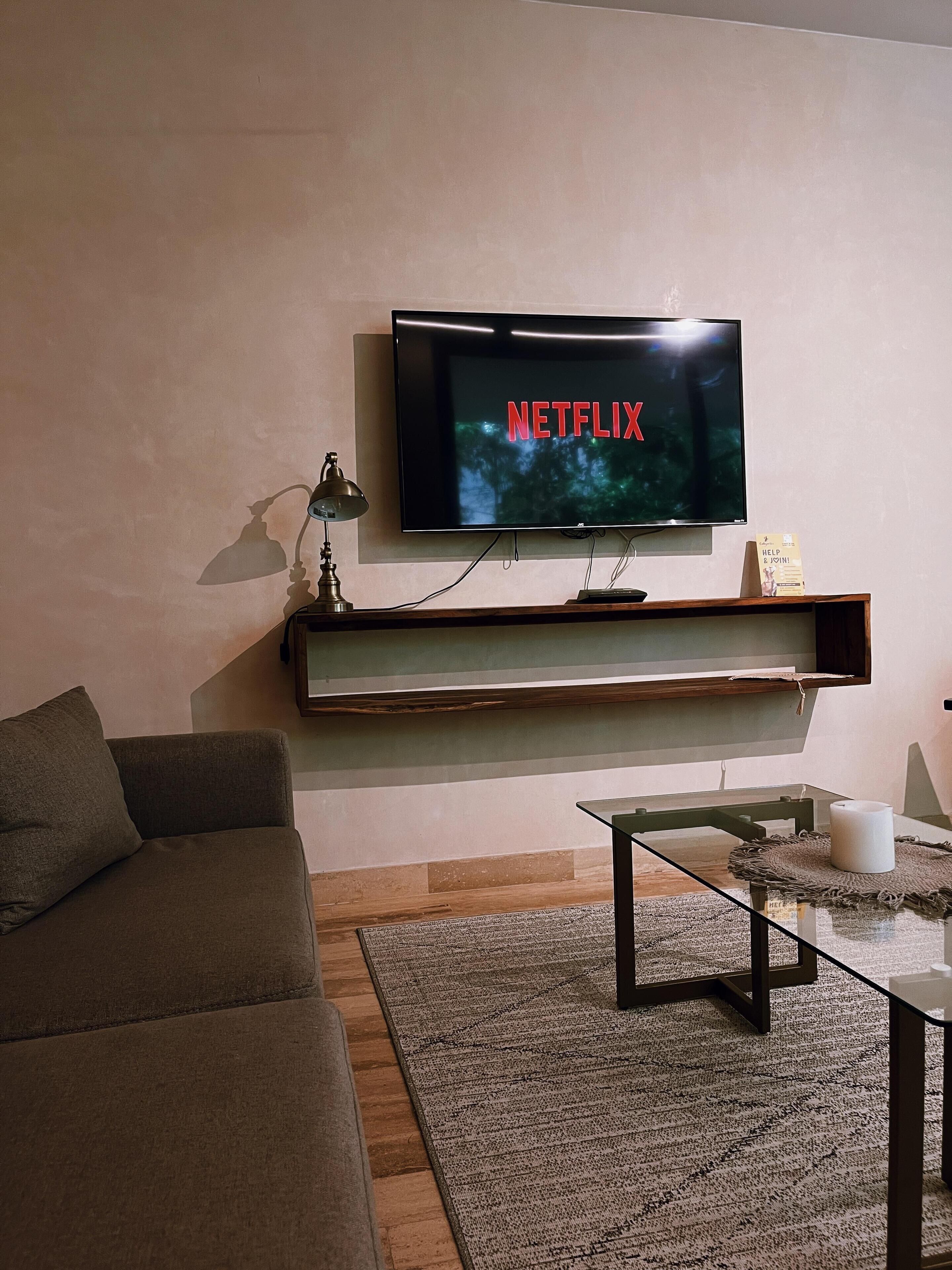 Una sala de estar con un televisor de pantalla plana montado en la pared, un sofá, una mesa de centro y una alfombra.