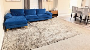 A living room with a blue sectional sofa, a fluffy rug, a small wooden side table, and two abstract paintings on the wall. - Cozy 2-bedroom bungalow in cozy East Point GA 15 mins from downtown Atlanta (East Point)