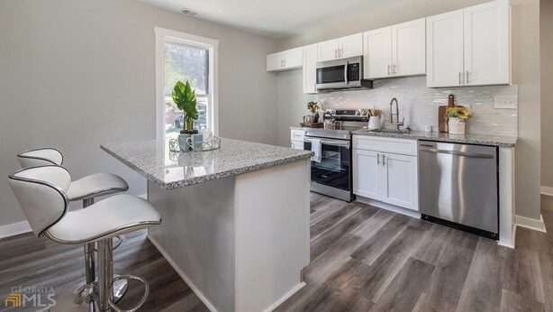 A modern kitchen with white cabinets, stainless steel appliances, and a granite countertop island. - Cozy 2-bedroom bungalow in cozy East Point GA 15 mins from downtown Atlanta (East Point)