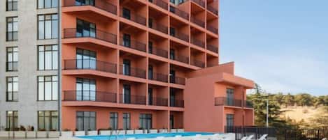 Ein mehrstöckiges Hotel mit Balkonen, einem Schwimmbad und Liegestühlen.
