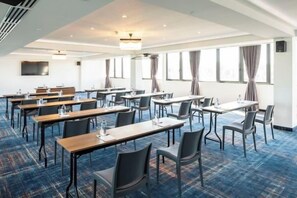 A conference room with tables and chairs arranged for meetings, large windows with curtains, and a flat-screen TV mounted on the wall. - Gino Seaside Tbilisi, Trademark Collection by Wyndham (Tbilisi)