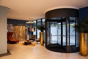 A lobby with a revolving door, seating area, and large potted plants.