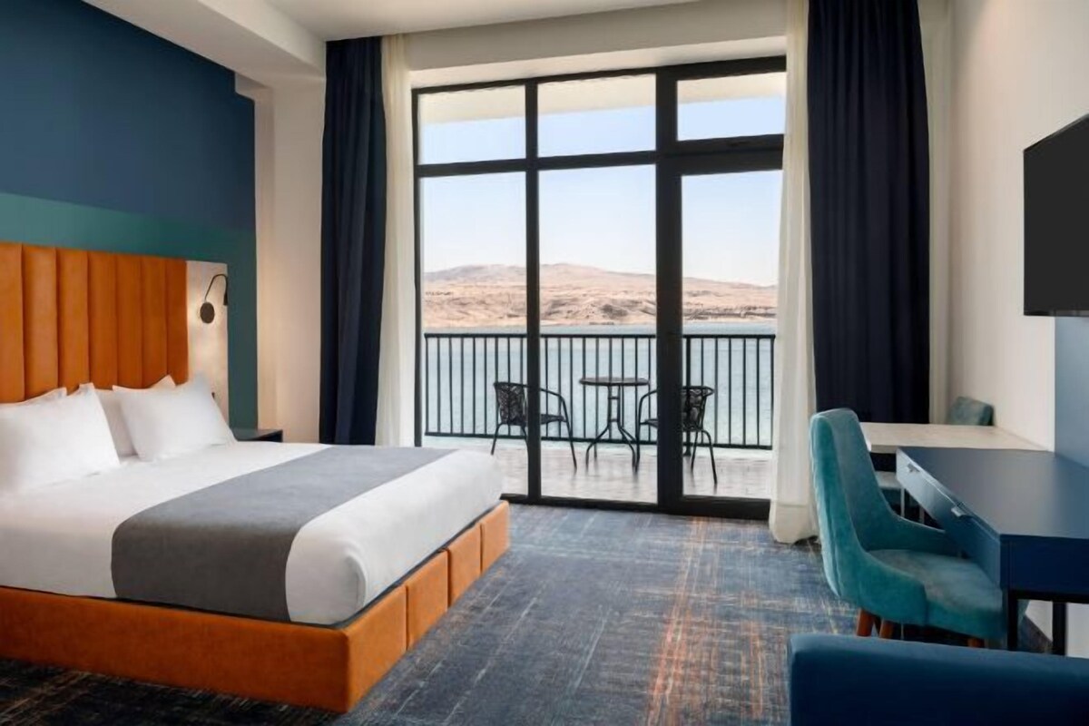 Een hotelkamer met een groot bed, een bureau en een balkon met uitzicht op het landschap.