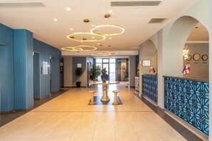 A hotel lobby with a reception desk, a plant, and a patterned wall.