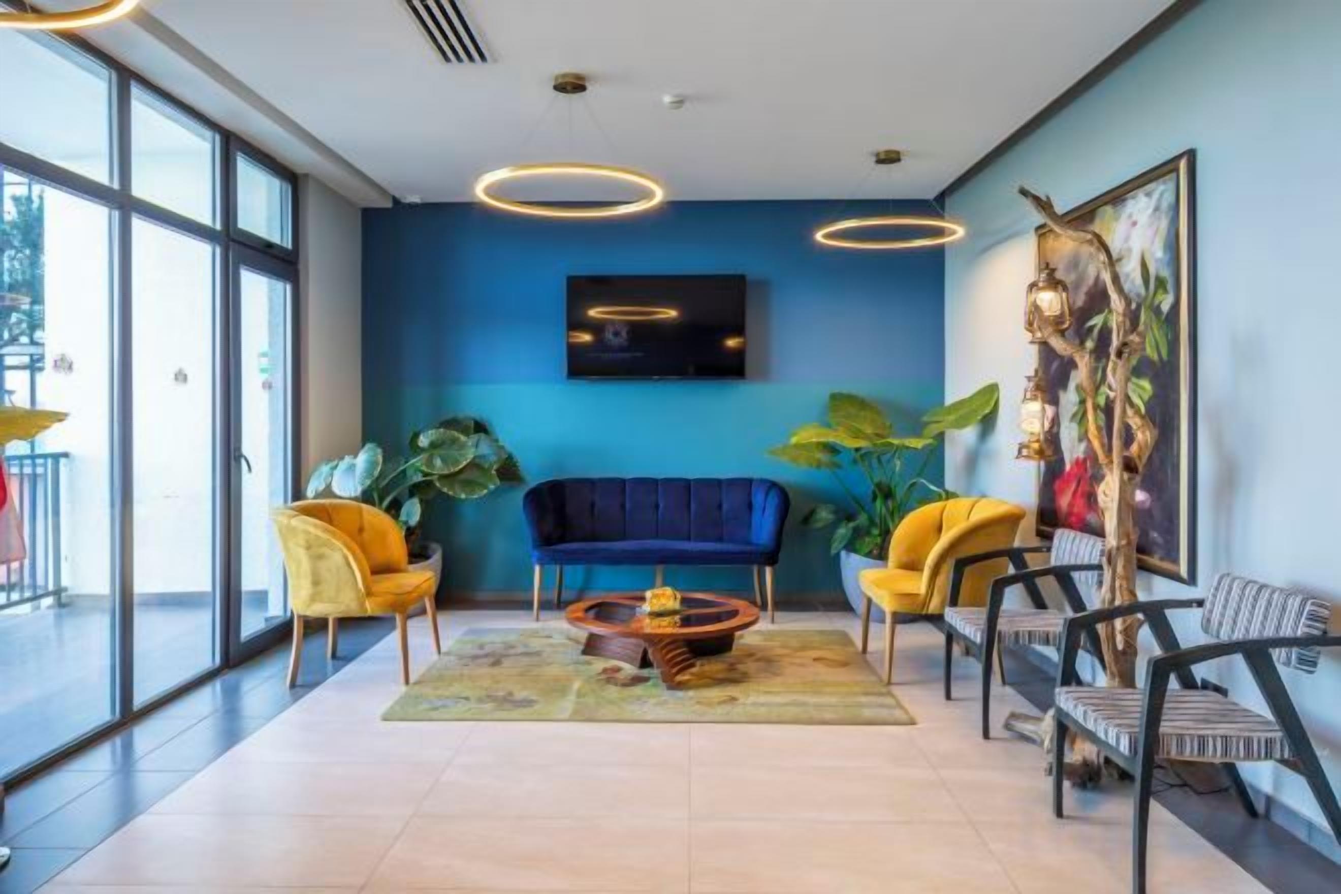 Een moderne loungehoek met een blauwe wand, een bank, gele stoelen en een salontafel.