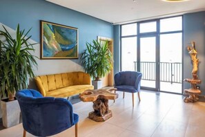 A modern lounge area with a yellow sofa, blue chairs, a wooden coffee table, and large windows. - Gino Seaside Tbilisi, Trademark Collection by Wyndham (Tbilisi)