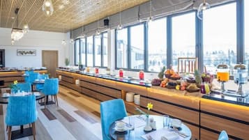 A modern restaurant with a long counter, blue chairs, and a view of the city.