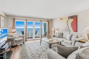 A modern hotel room with a balcony, a flat-screen TV, a sofa, a coffee table, and a large abstract painting.