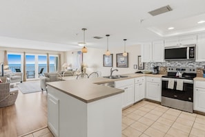 A modern kitchen with white cabinets, a central island, stainless steel appliances, and a view to the outside.