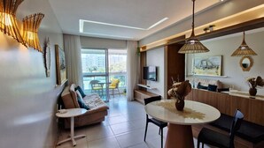 A modern living room with a sofa, a dining table, and a TV. There is a balcony with a view of buildings. - COJOC0100 - Cond Torres do Atlântico (Lauro de Freitas)