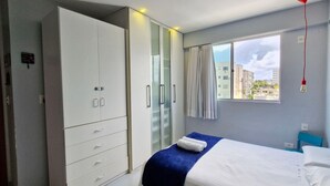 A hotel room with a bed, a wardrobe, a window with curtains, and a view of buildings outside. - COJOC0100 - Cond Torres do Atlântico (Lauro de Freitas)
