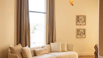 A modern living room with a sectional sofa, a wooden coffee table, a woven chair, and a large window with curtains.