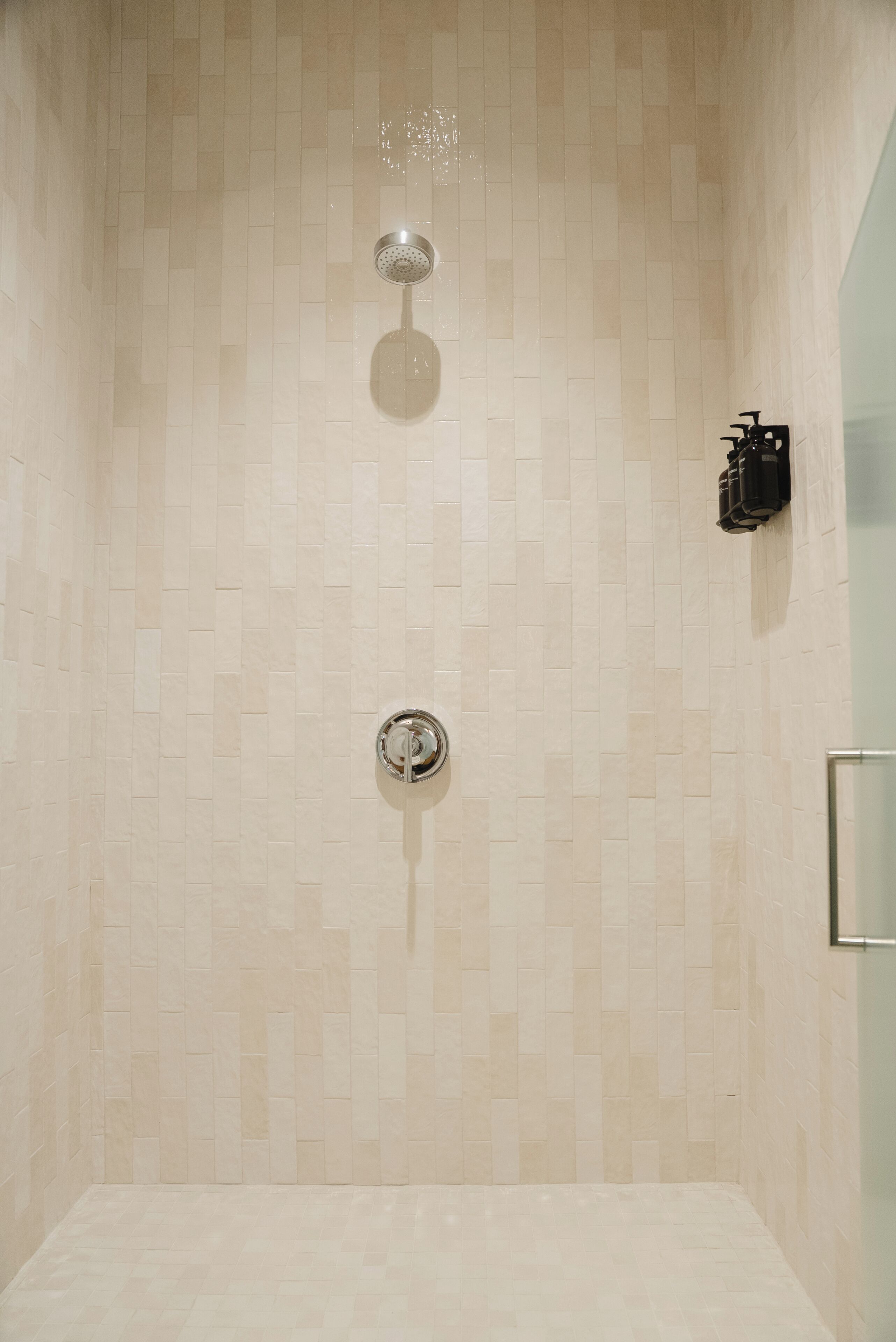 A shower with a tiled wall, a handheld showerhead, and a wall-mounted faucet.
