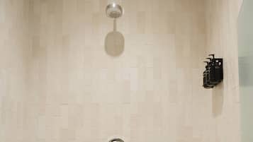 A shower with a tiled wall, a handheld showerhead, and a wall-mounted faucet.