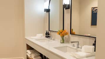 A modern bathroom with two sinks, a large mirror, and a wooden shelf with towels.