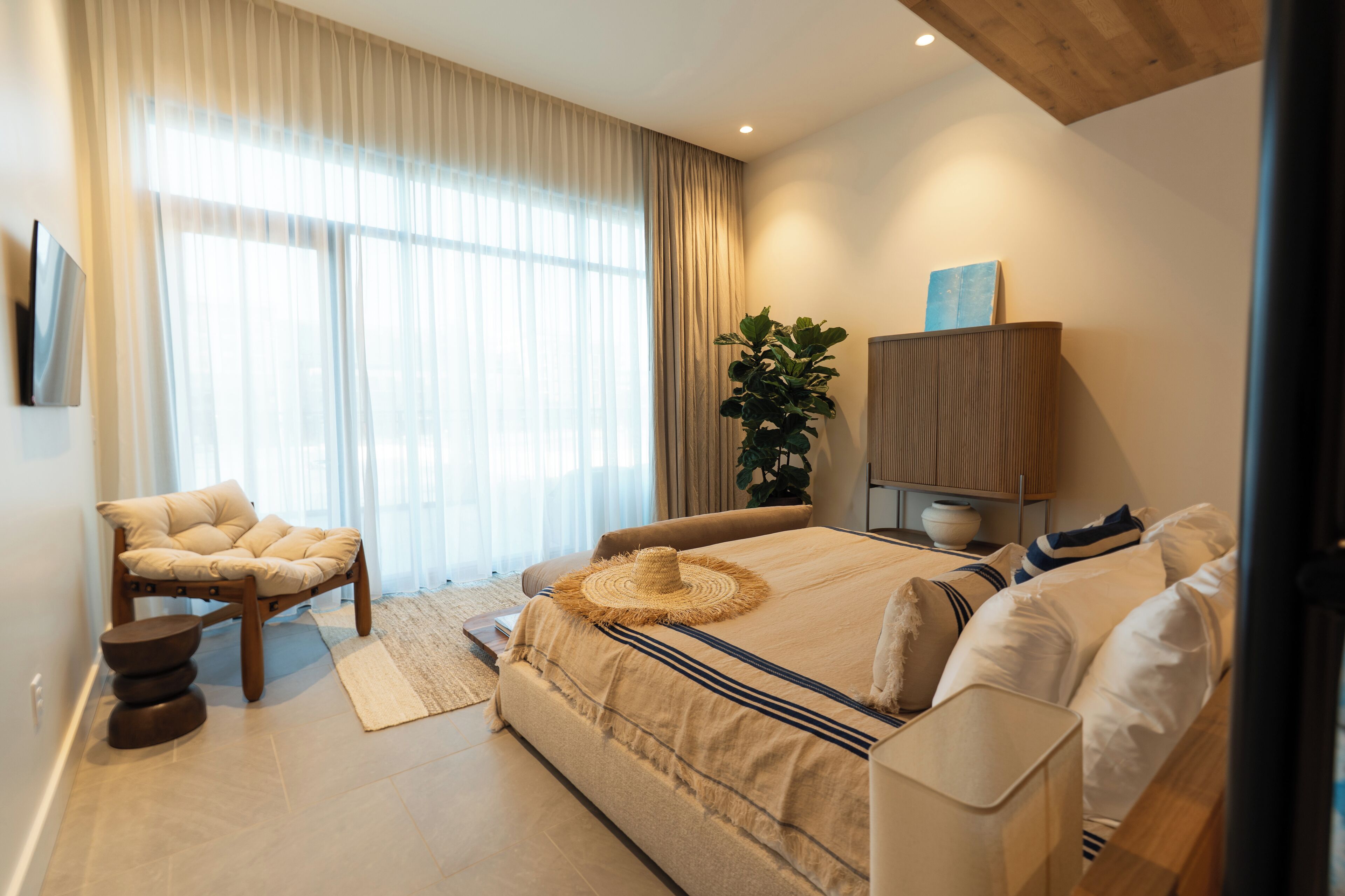 Une chambre moderne avec un grand lit, une chaise, une plante et un meuble.