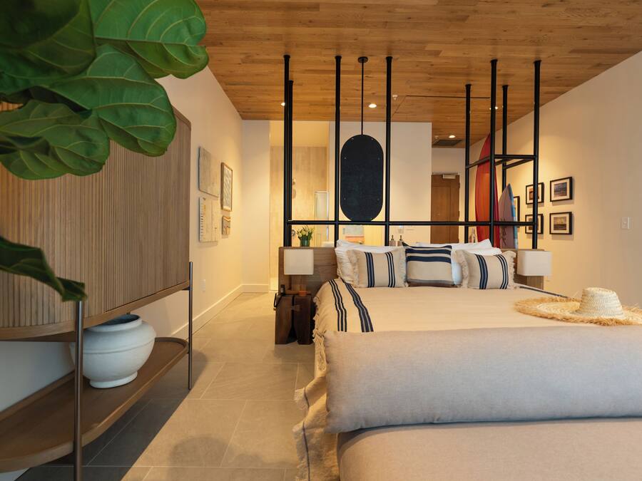 A modern bedroom with a wooden ceiling, a large bed with striped bedding, a bedside table, and a plant.
