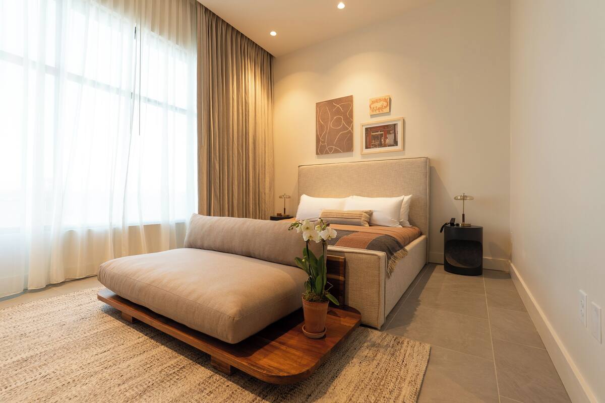 Une chambre moderne avec un canapé-lit, une table de chevet, une lampe et une orchidée en pot.
