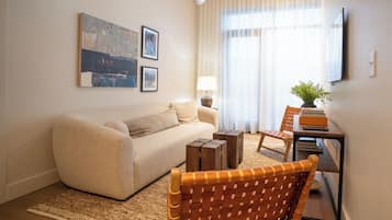A living room with a sofa, a coffee table, a dining table with chairs, a lamp, and artwork on the wall.