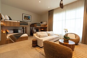 A modern hotel room with a bunk bed, a sofa, a round wicker chair, and a small table with a plant. - The Sitio (Virginia Beach)
