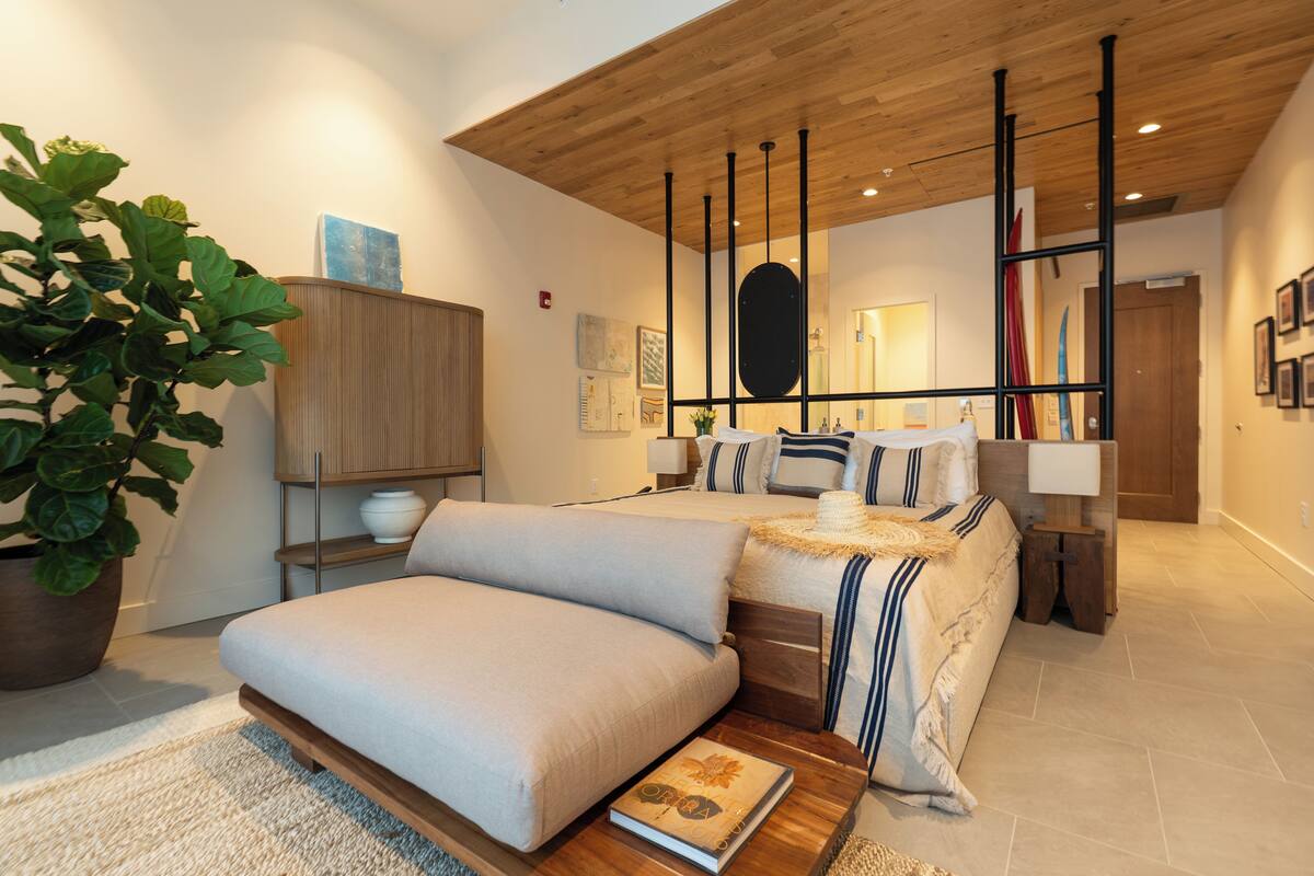 Une chambre à coucher moderne avec un grand lit, une table de chevet, une commode, une plante en pot et un plafond en bois.