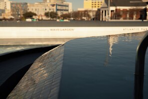 A waterfront promenade with a metal railing, a sign reading 'Wavegarden,' and buildings in the background. - The Sitio (Virginia Beach)