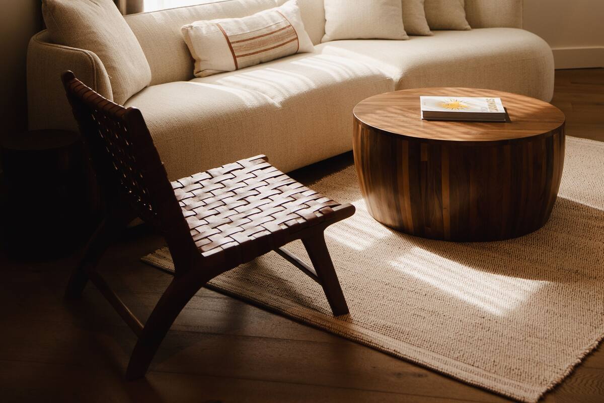 Un salon comprenant un canapé, une table basse en bois, un fauteuil en osier et un luminaire suspendu.