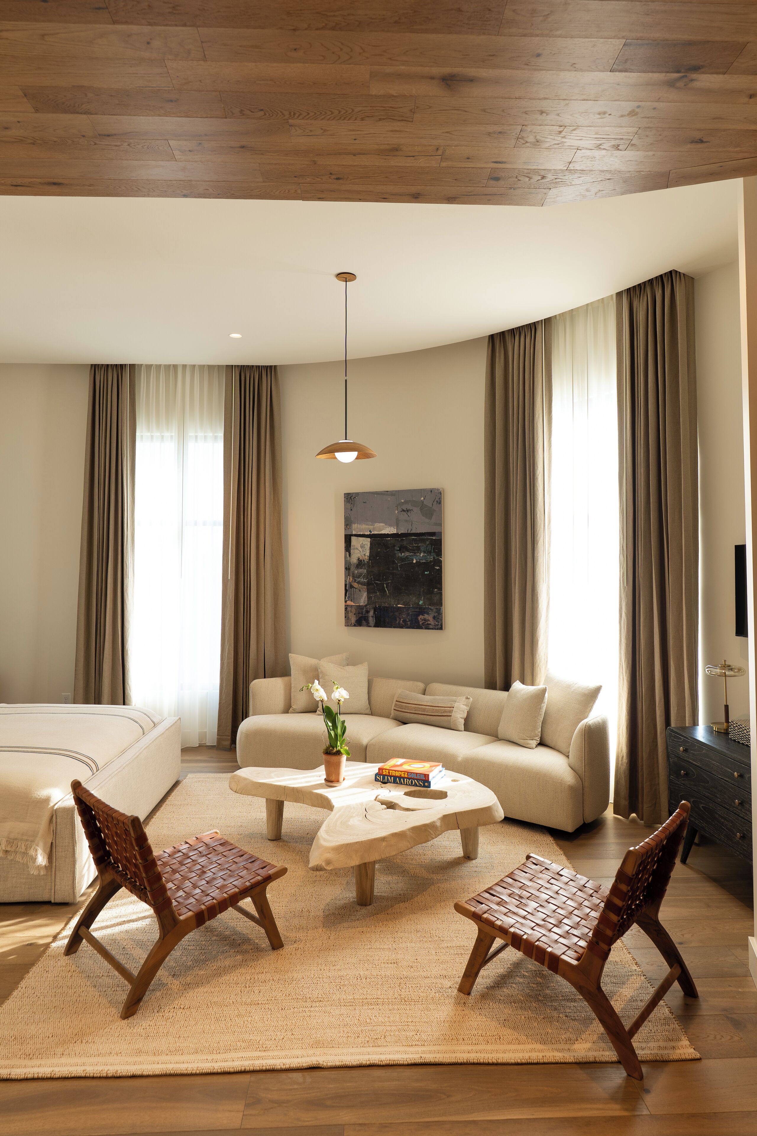 Una habitación de hotel moderna con techo de madera, una cama grande, un sofá, dos sillas de madera, una mesita de centro y un cuadro en la pared.